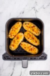 Twice baked potatoes in an air fryer basket, topped with shredded cheese and bacon.