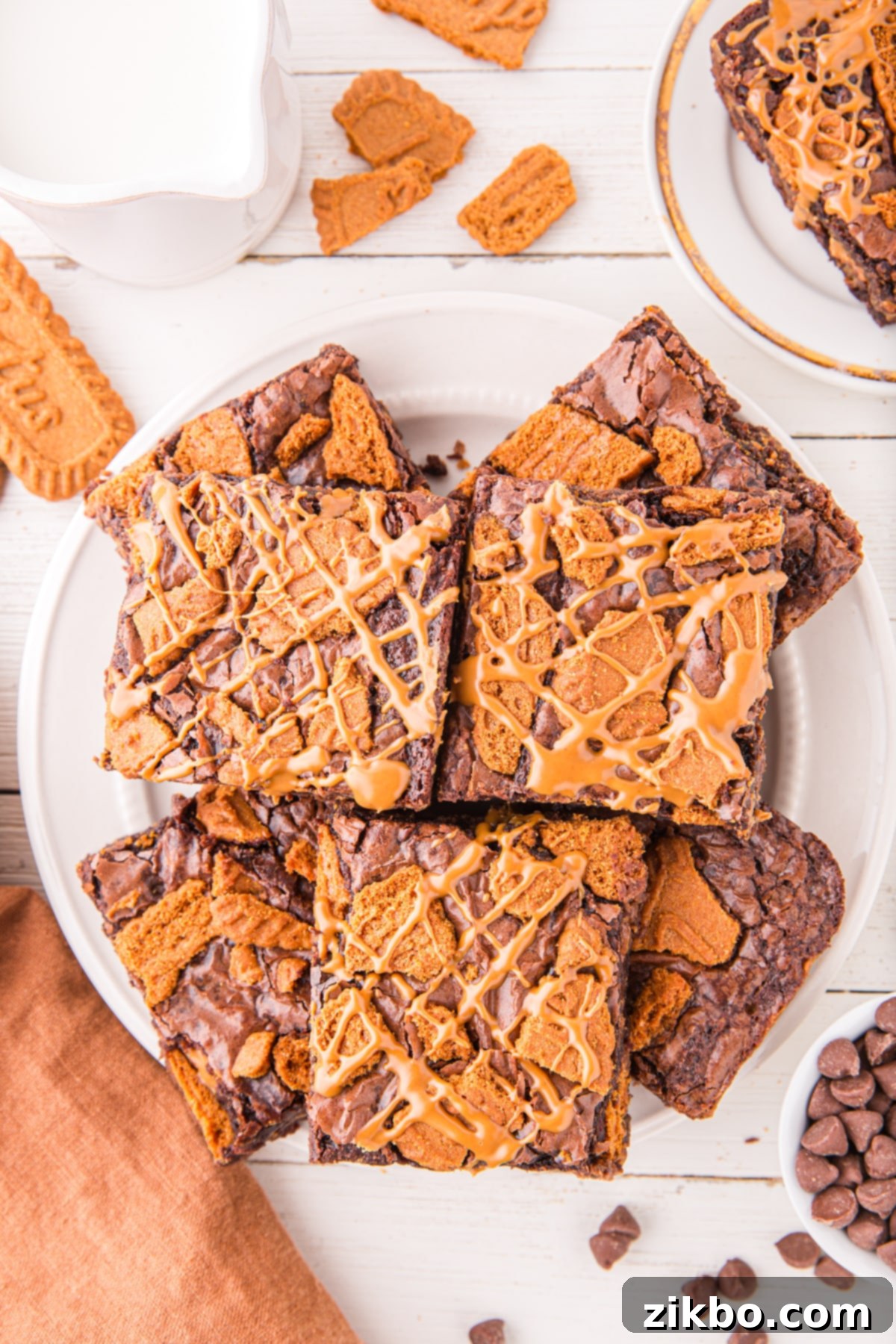 A plate featuring a stack of three fudgy Biscoff brownies, garnished with a drizzle of cookie butter and a few Biscoff cookie pieces, highlighting the layers and rich topping.