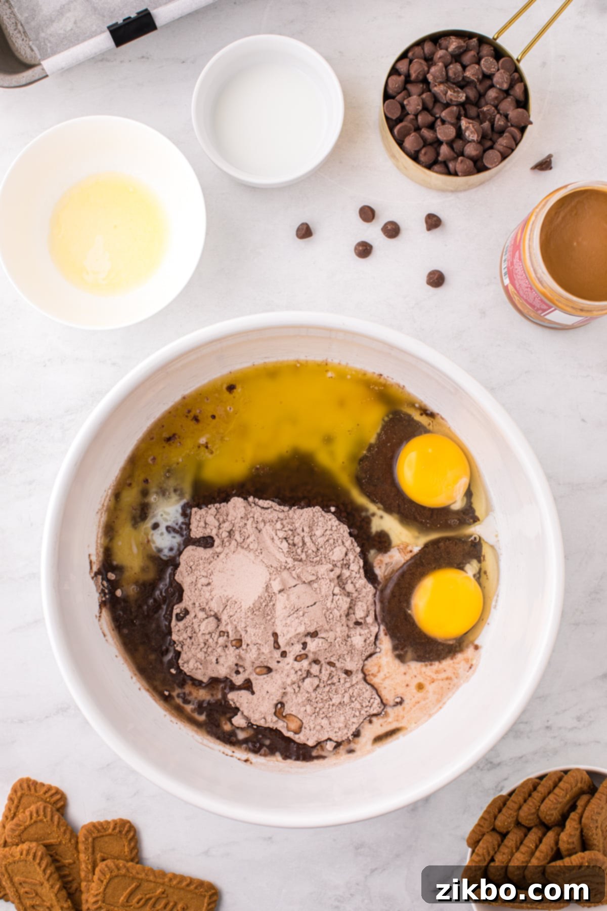 A mixing bowl containing brownie mix, two eggs, a splash of milk, and melted butter, ready to be combined.