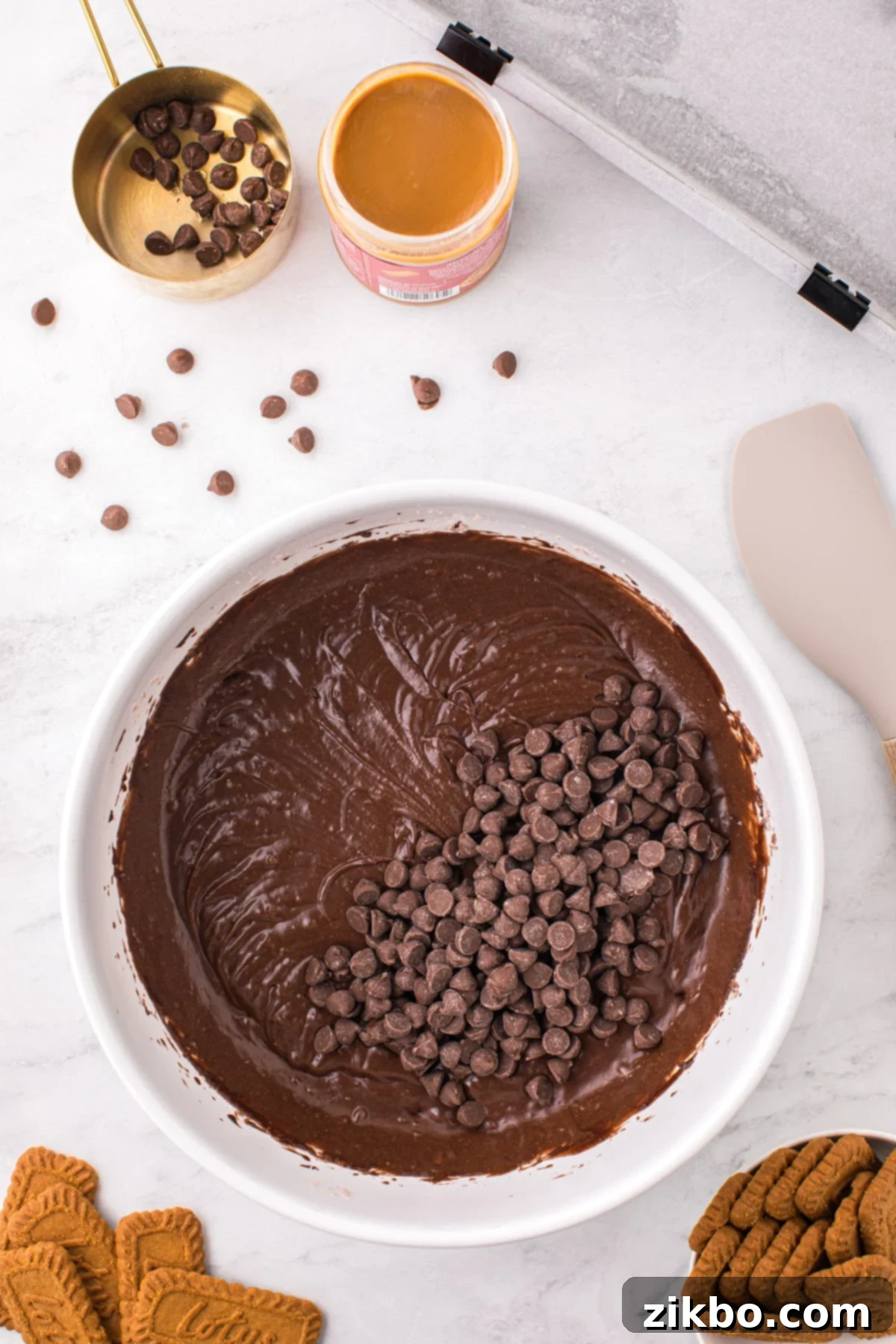 A bowl of rich chocolate brownie batter, with milk chocolate chips carefully folded in, ready for baking.