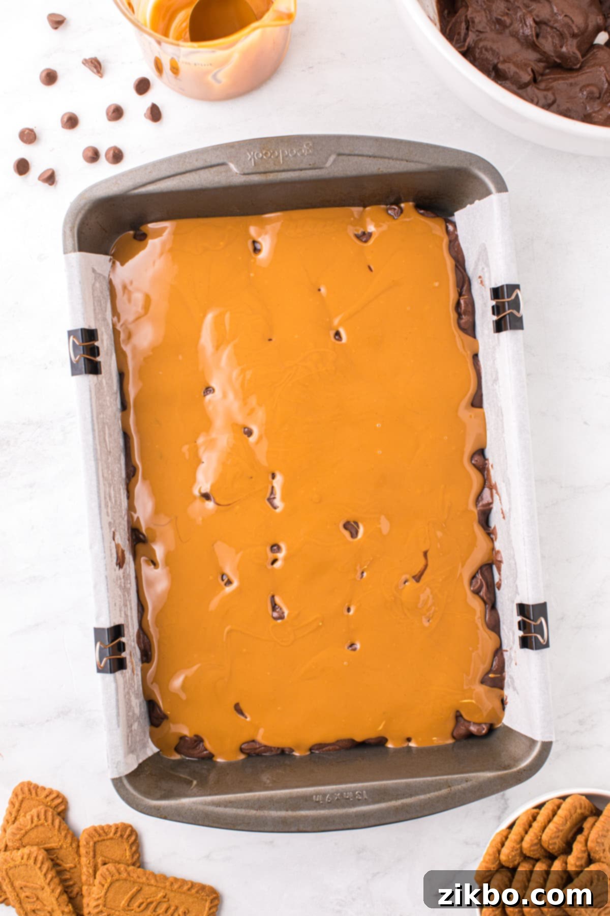 A baking pan with a brownie batter base, topped with dollops of creamy Biscoff cookie butter, ready for spreading.