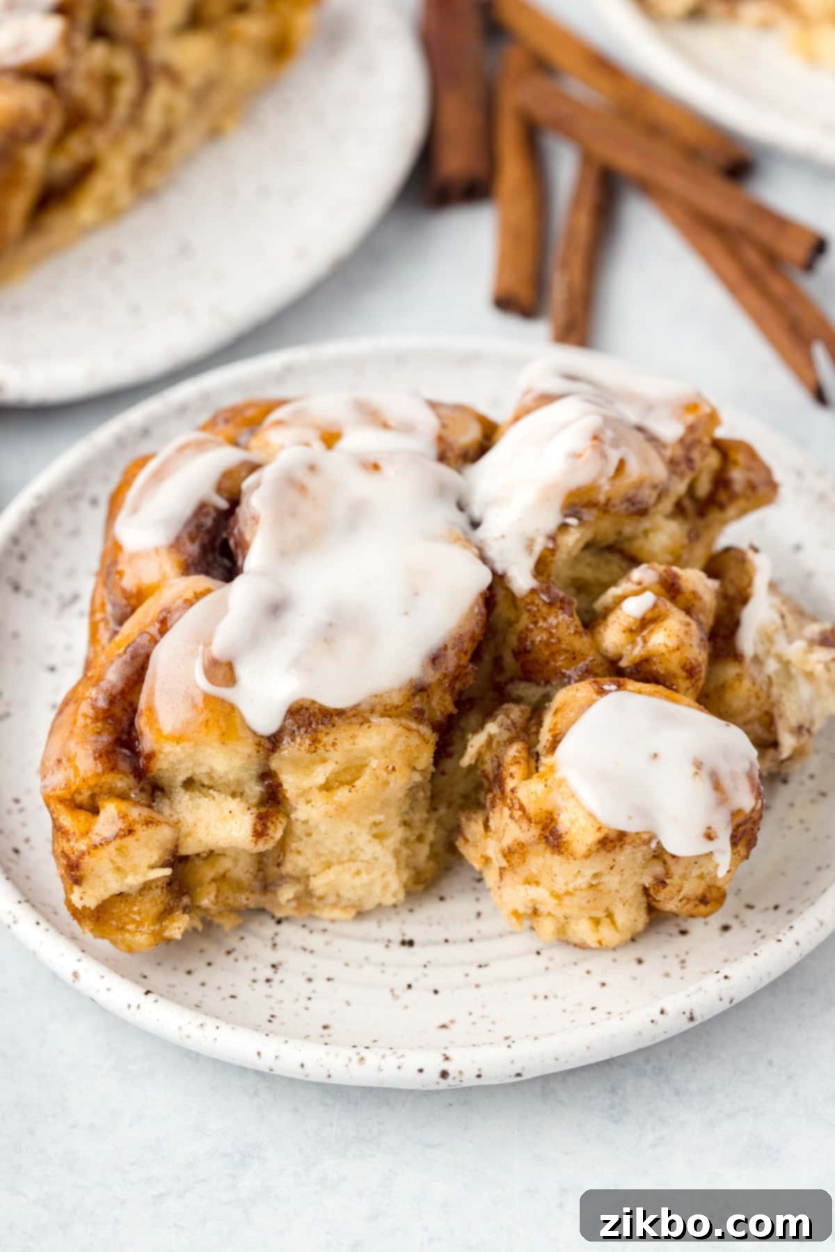 A serving of warm cinnamon roll casserole on a plate, generously topped with melted icing.