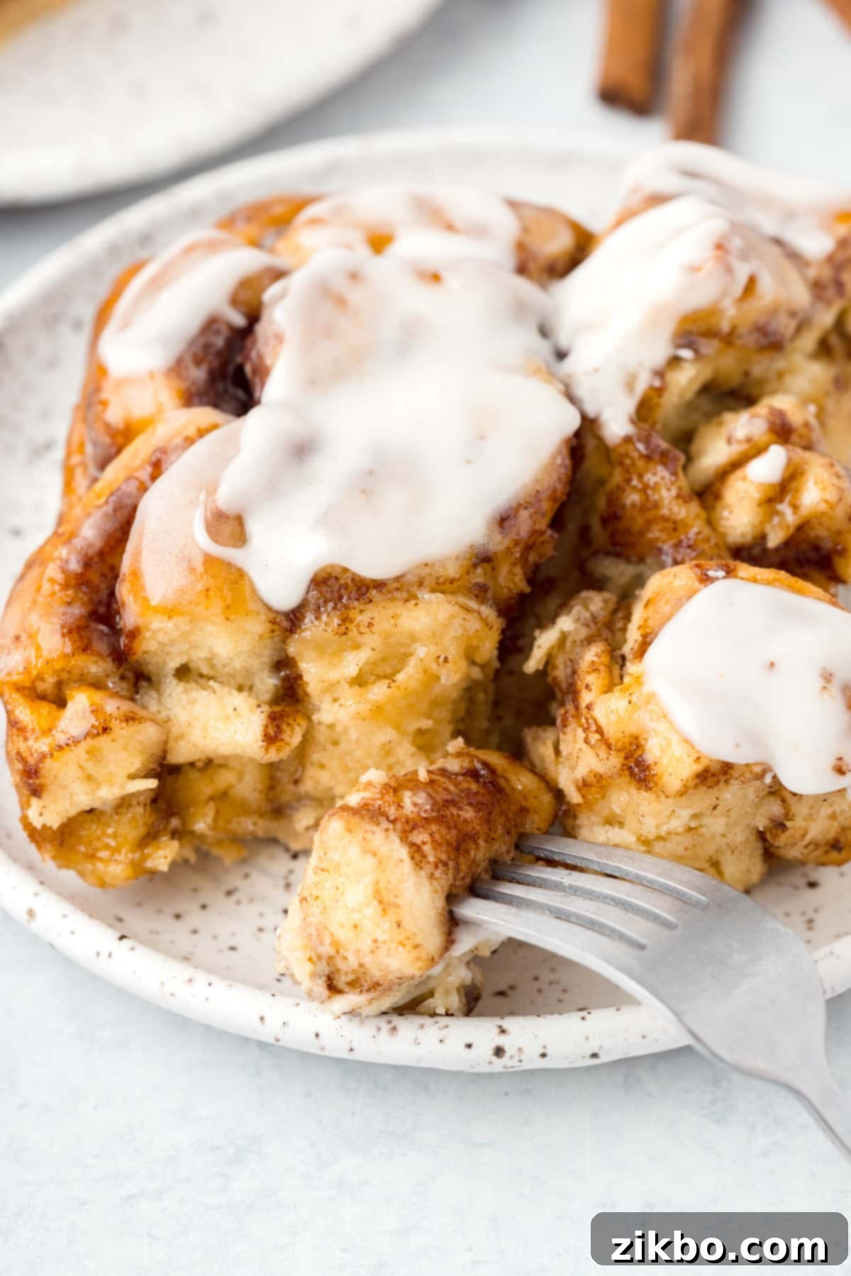 A fork taking a delicious, gooey portion from a baked cinnamon roll casserole, showing the soft, custardy interior.