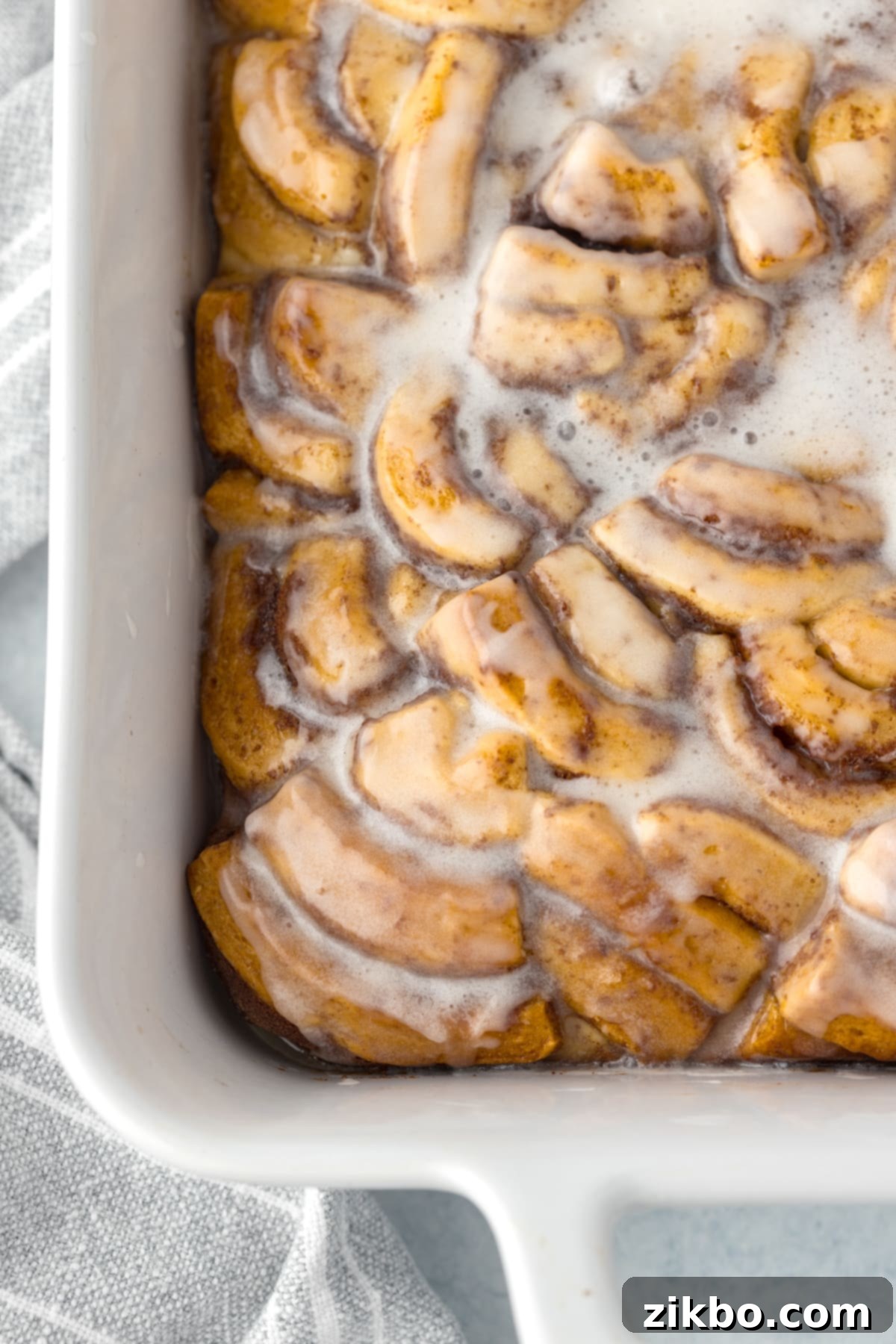 A baking dish filled with a golden-brown cinnamon roll casserole, perfectly baked and generously topped with melted icing.