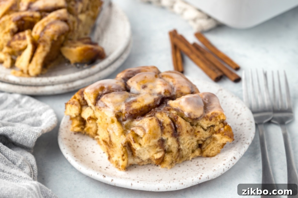 A generous serving of cinnamon roll bake on a white plate, showcasing its soft interior and gooey icing.
