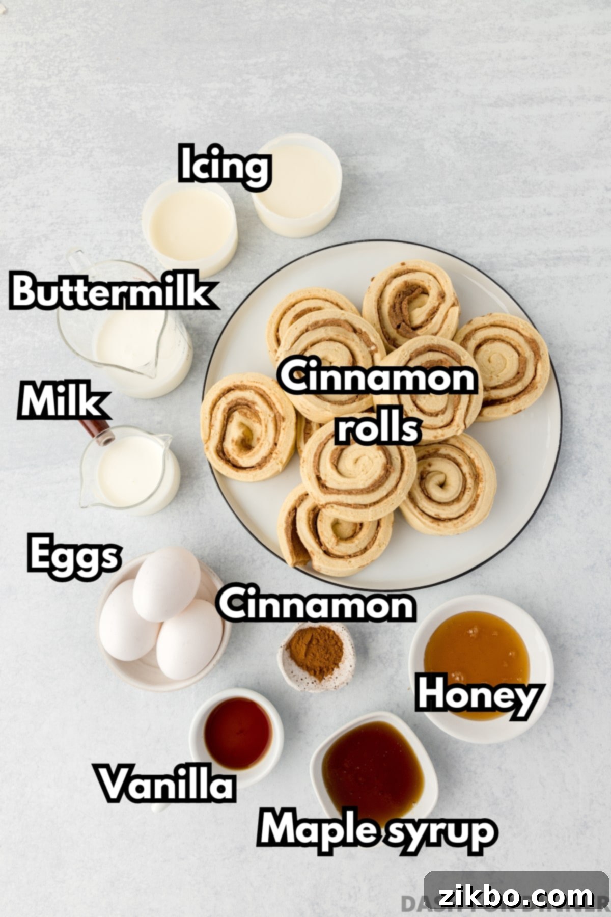 A visual display of all the ingredients needed to make the easy cinnamon roll casserole: refrigerated rolls, maple syrup, honey, milk, eggs, vanilla, and cinnamon.