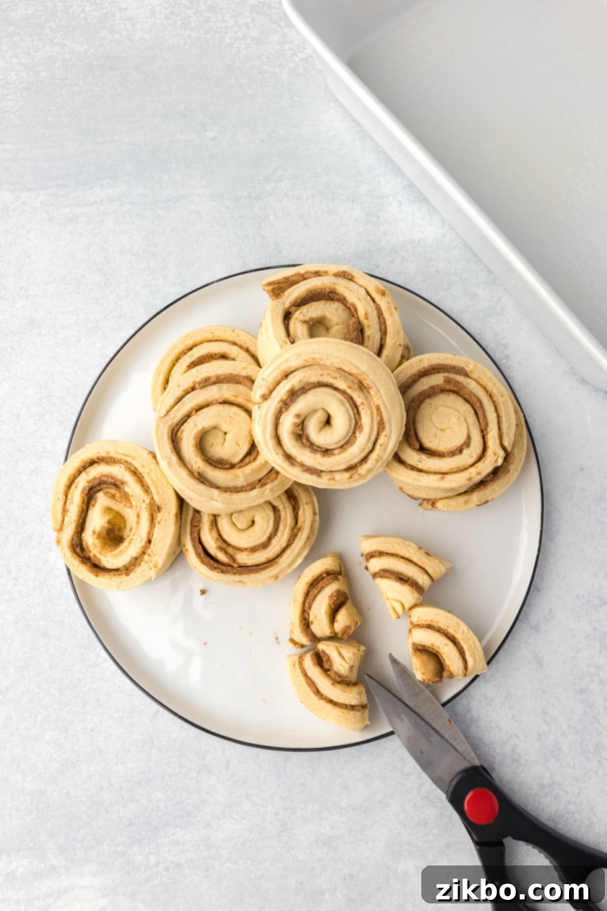 Slicing canned cinnamon rolls into quarters with kitchen scissors.