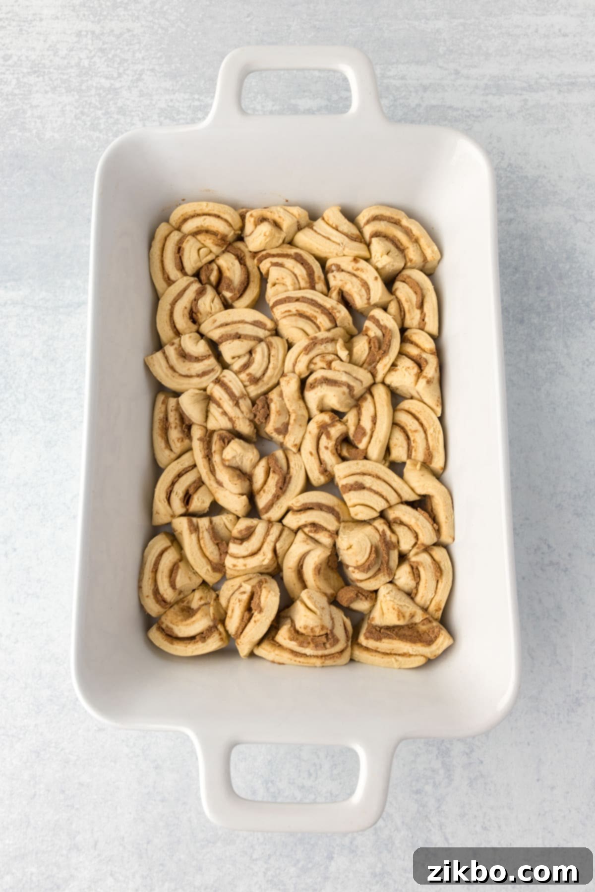 A casserole dish with cinnamon rolls sliced and arranged evenly in the dish.