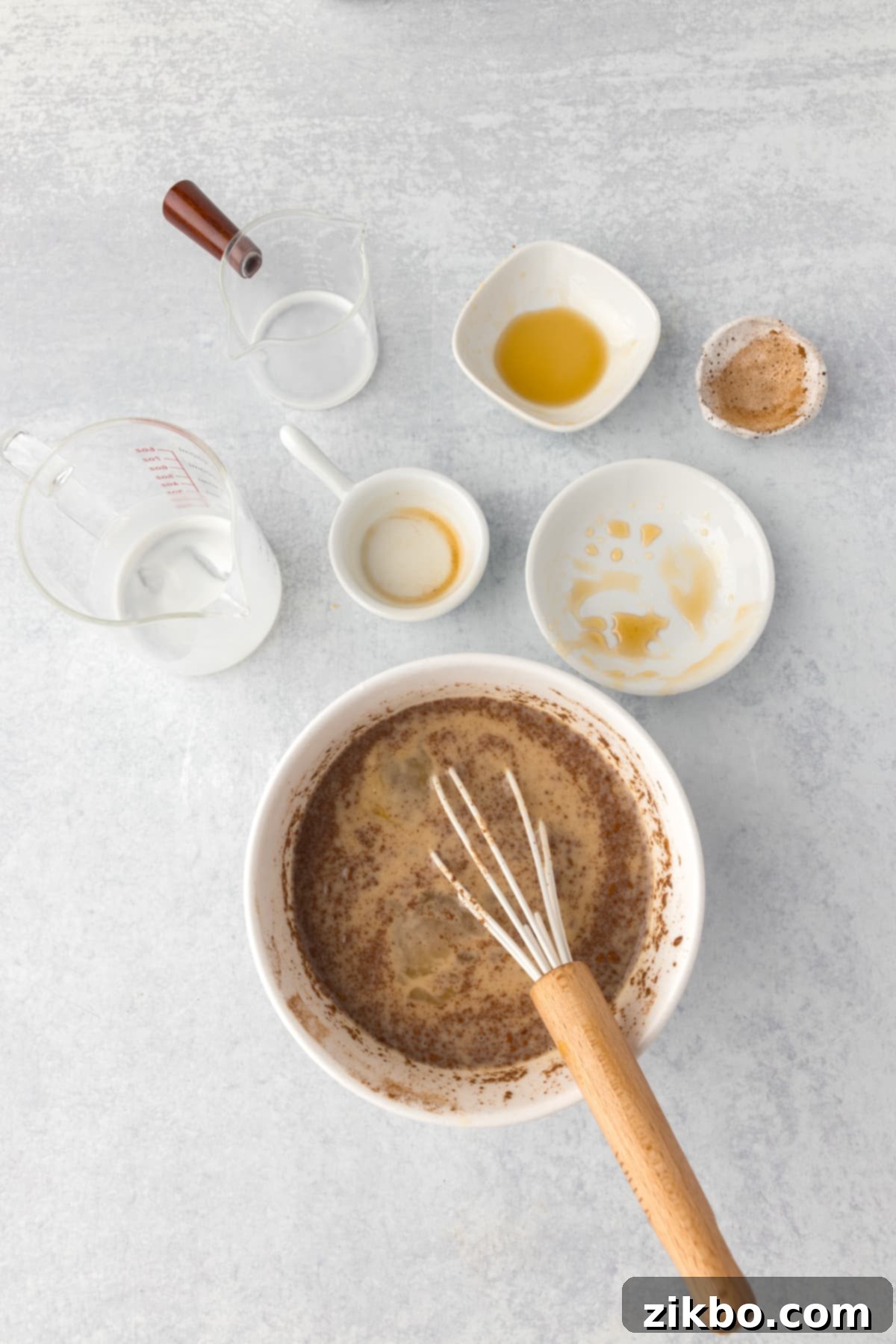 Whisking together the eggs, milk, buttermilk, honey, maple syrup, vanilla, and cinnamon in a bowl.