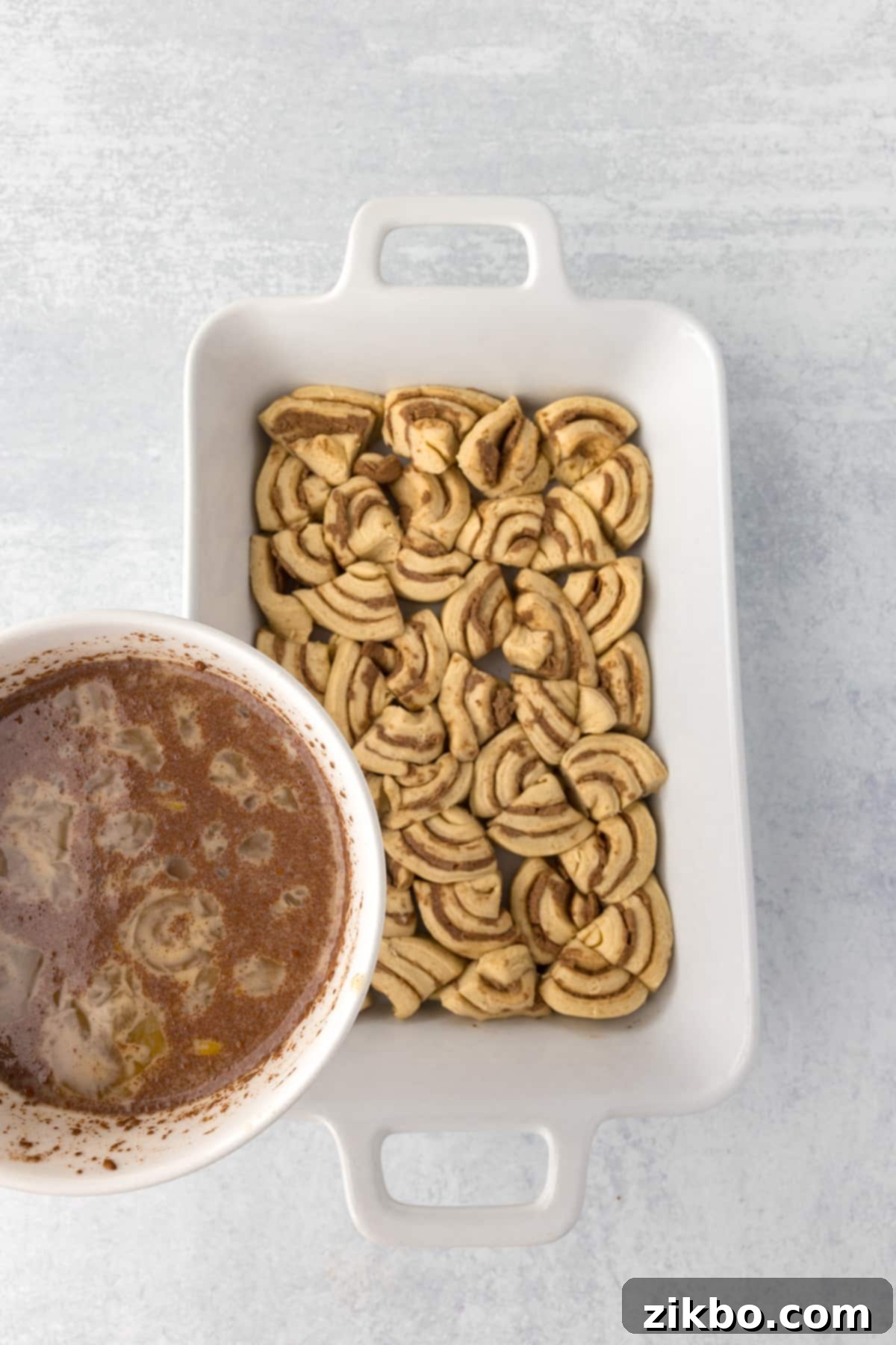 Pouring the prepared custard mixture evenly over the cinnamon roll pieces in the baking dish.