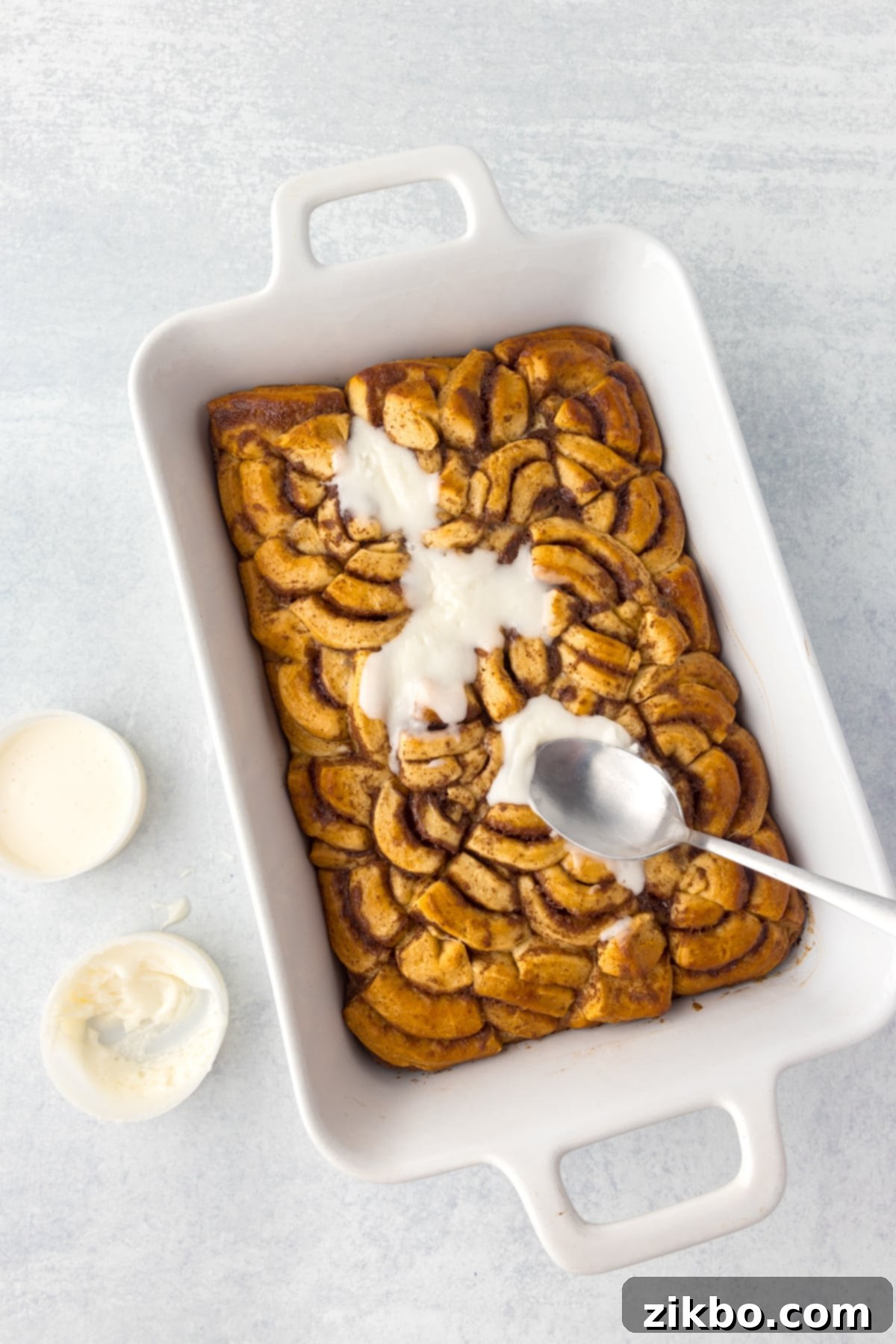 Spreading the delicious reserved icing over the freshly baked cinnamon roll casserole.
