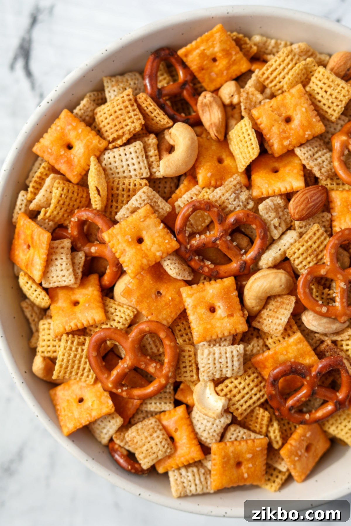 An overhead view of a bowl of snack mix with pretzels, crackers, cereal, and nuts.