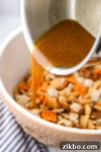 Pouring melted butter into a bowl of snack mix.