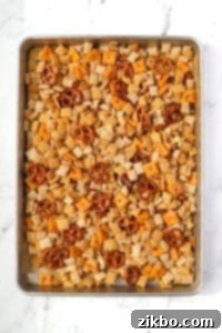 A baking sheet filled with snack mix with pretzels, cereal, and crackers.