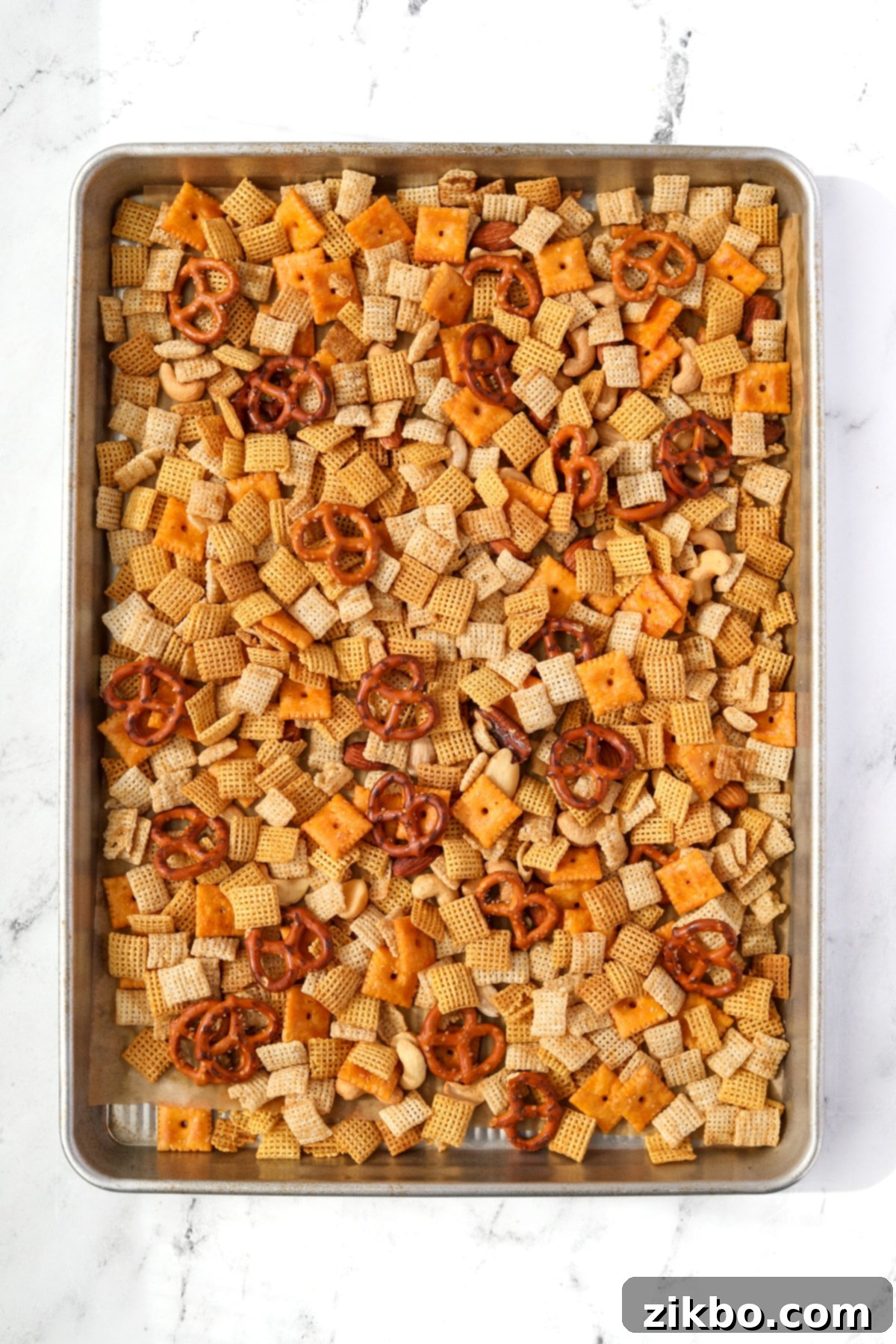 A baking sheet filled with snack mix with pretzels, cereal, and crackers.