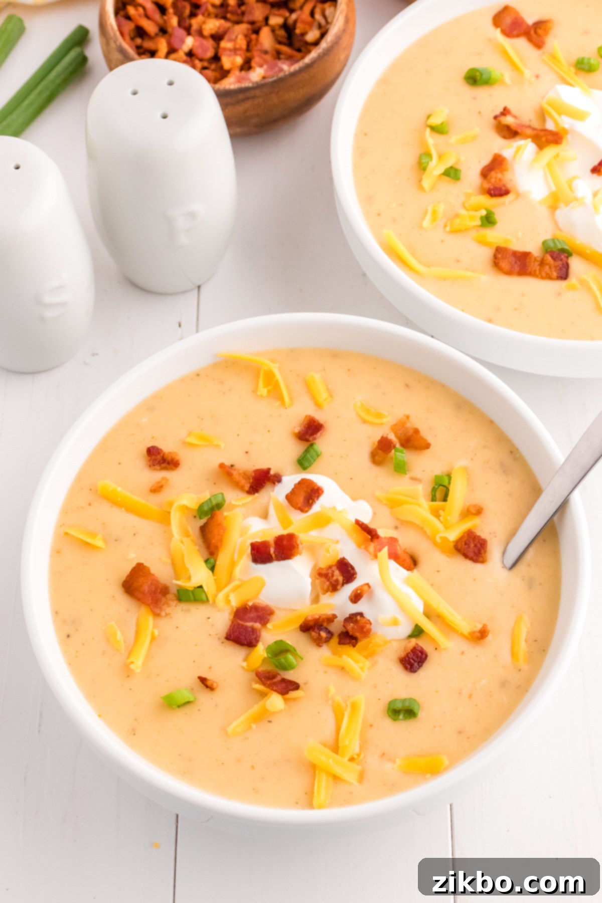 A perfectly garnished bowl of creamy loaded baked potato soup, topped with generous amounts of crispy bacon, shredded cheese, a swirl of sour cream, and fresh green onions.