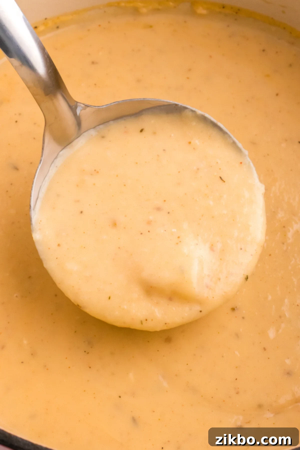 A ladle being dipped into a large pot of thick, creamy, cheesy potato soup, ready to be served.