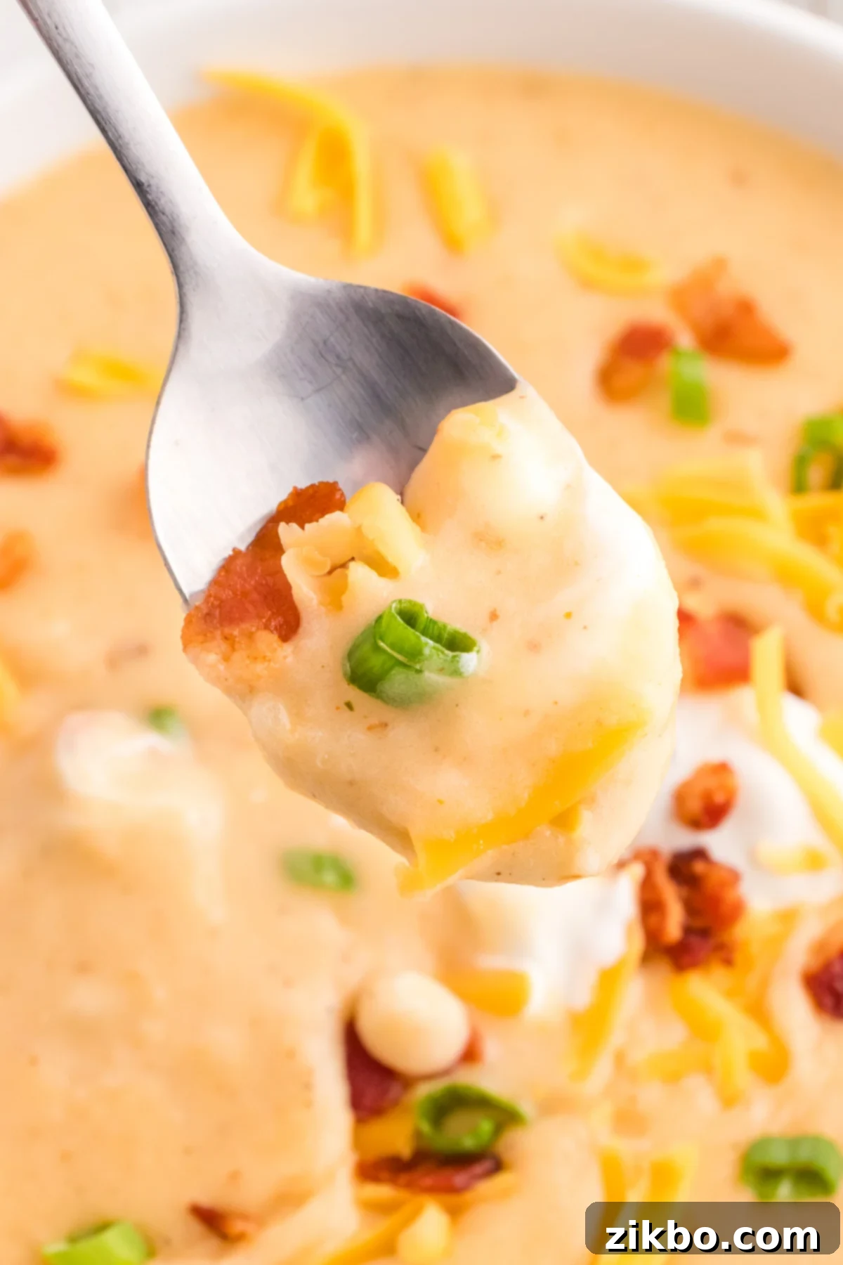 A spoon scooping creamy potato soup, garnished with bacon and green onions, showcasing its rich texture.