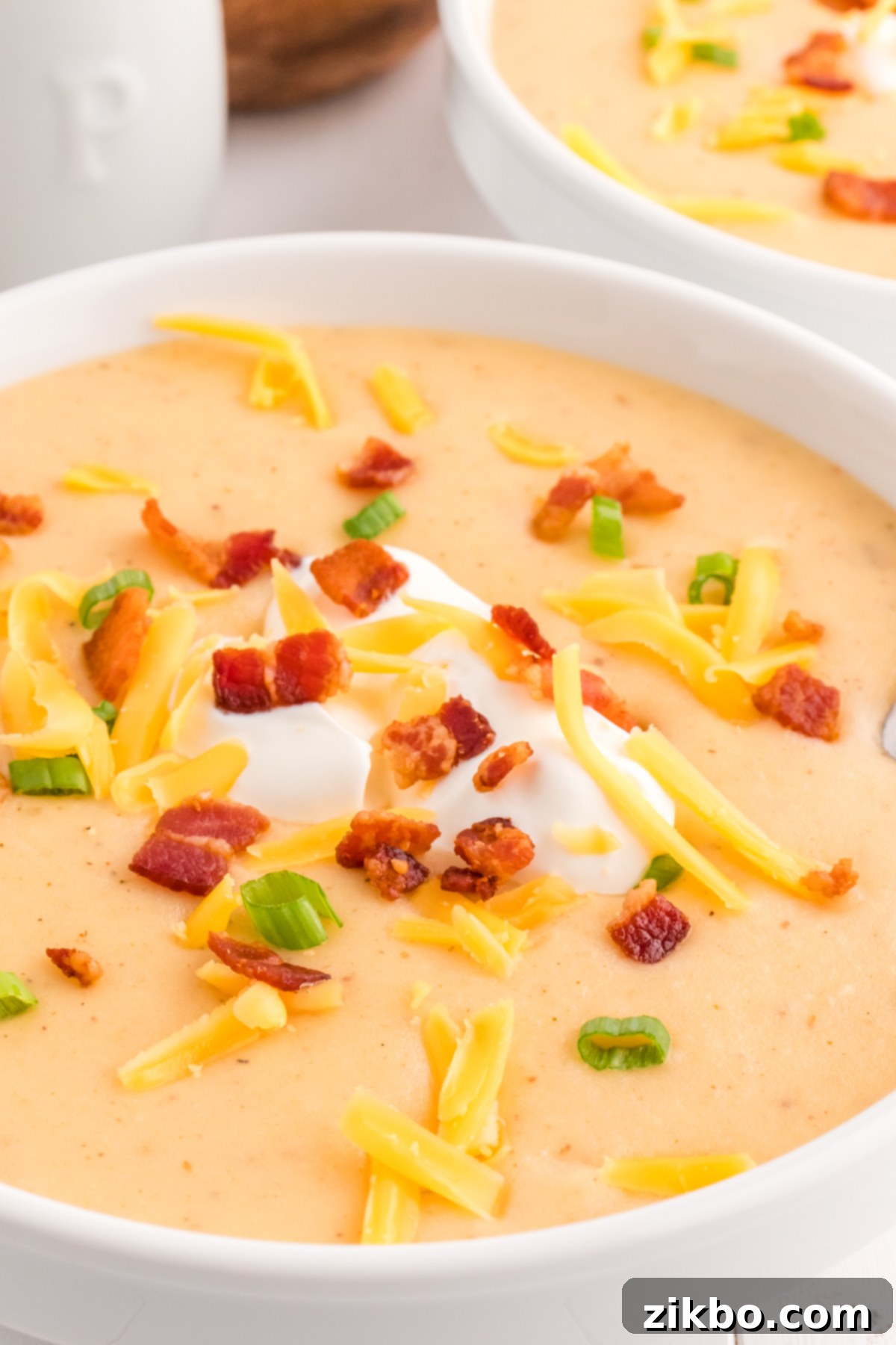 A close-up shot of a richly garnished bowl of loaded potato soup, featuring melted cheese, crispy bacon, and a swirl of sour cream, on a rustic surface.