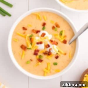 A bowl of rich, cheesy loaded baked potato soup topped with a swirl of sour cream, crispy bacon bits, and fresh green onions.