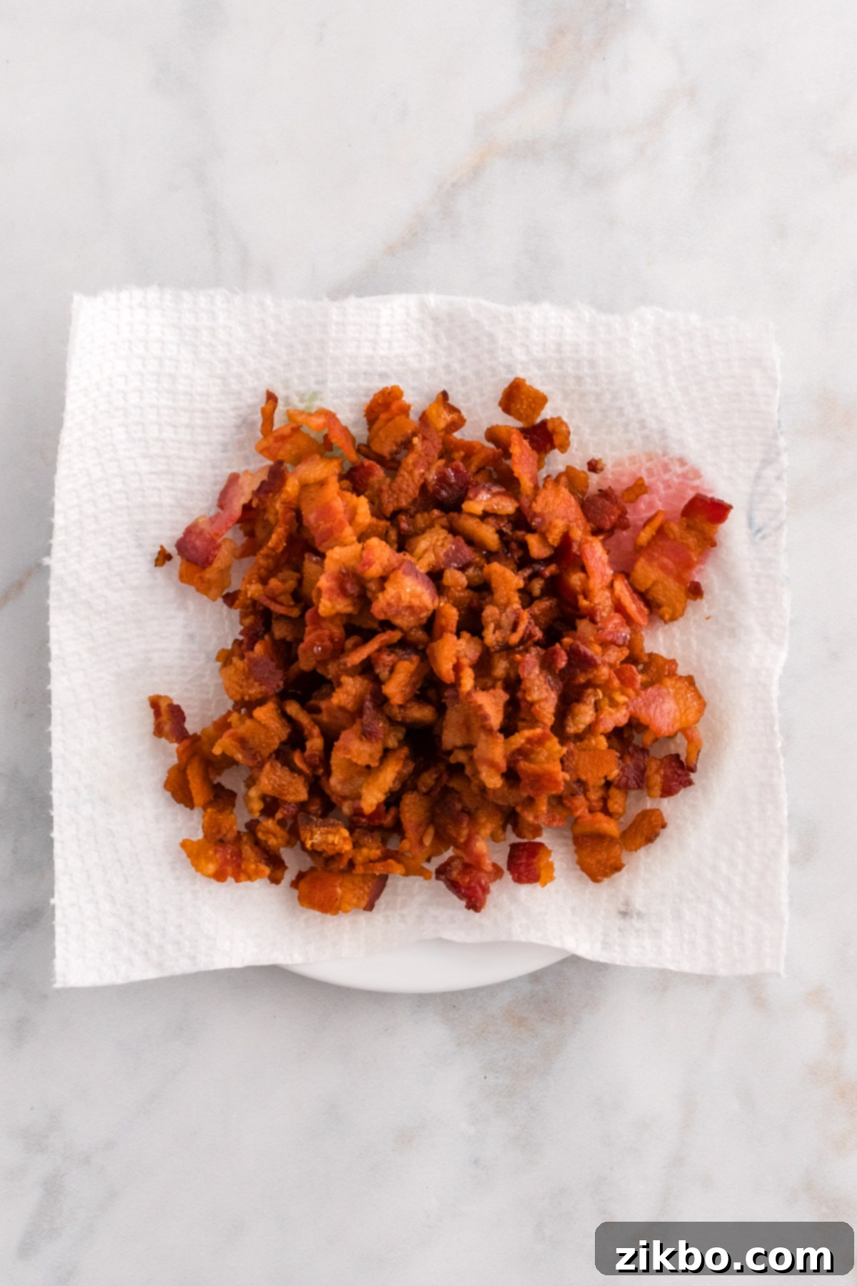 Crispy cooked bacon pieces draining on a paper towel-lined plate, ready to be crumbled as a topping.