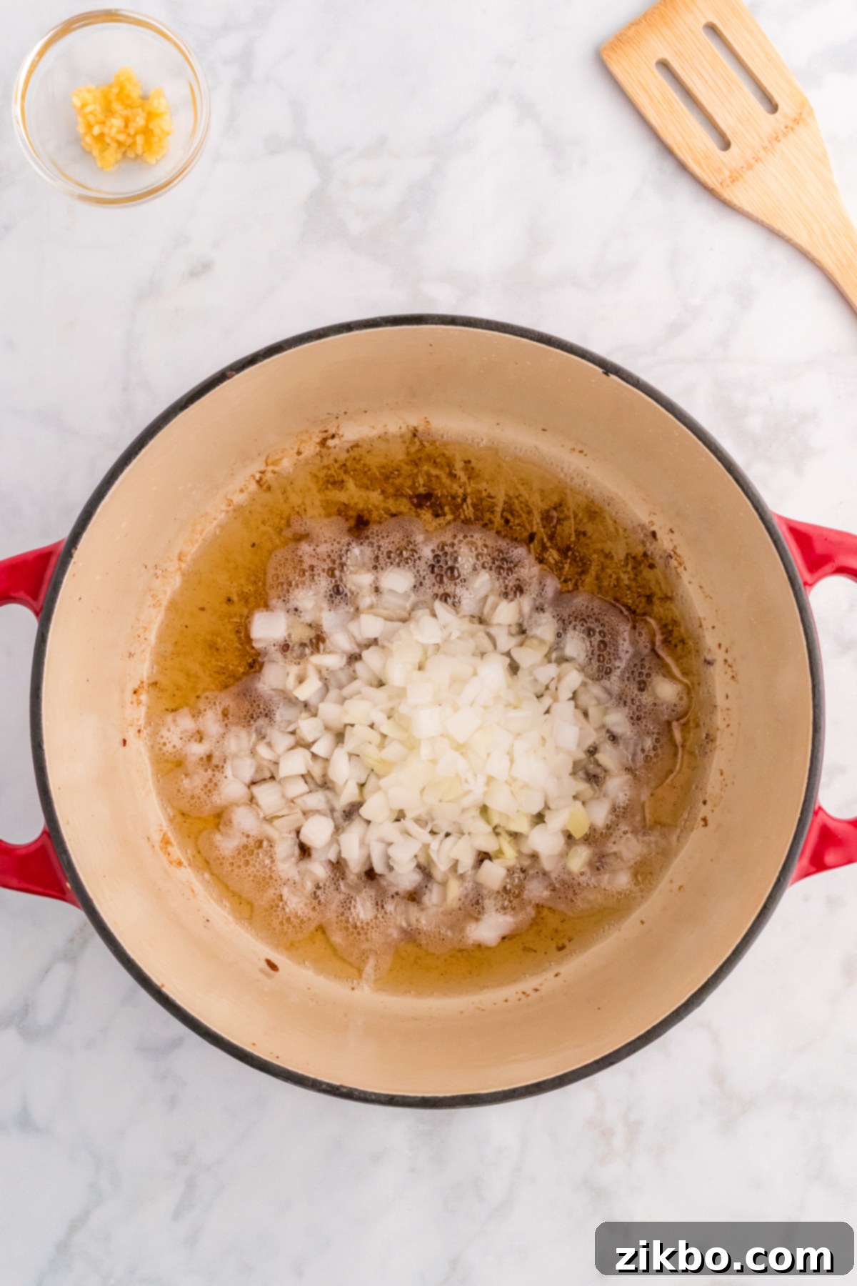 Diced onions simmering gently in bacon drippings within a Dutch oven, becoming translucent and flavorful.