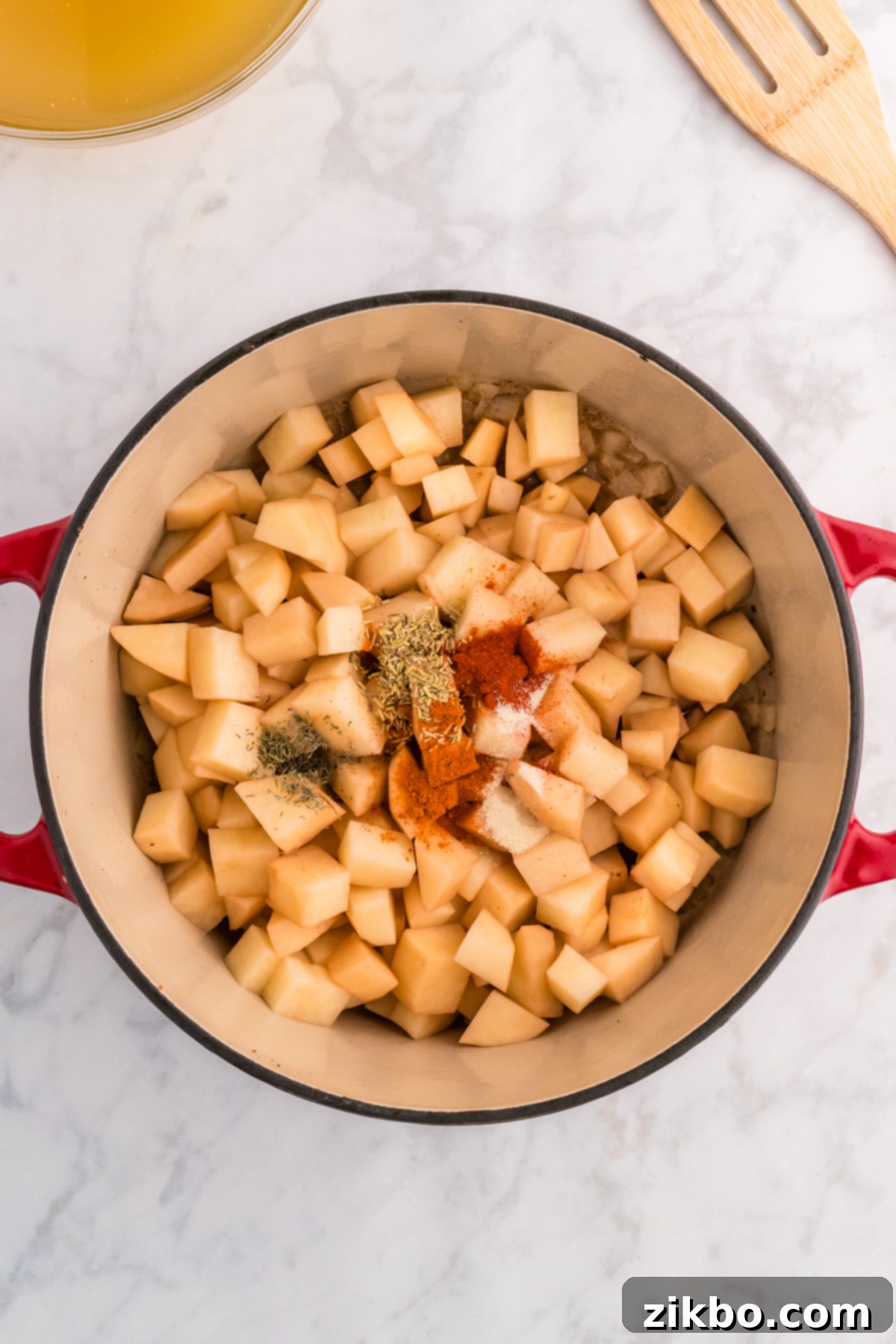 Cubed russet potatoes and a blend of savory seasonings being tossed in a Dutch oven with cooked onions and garlic.