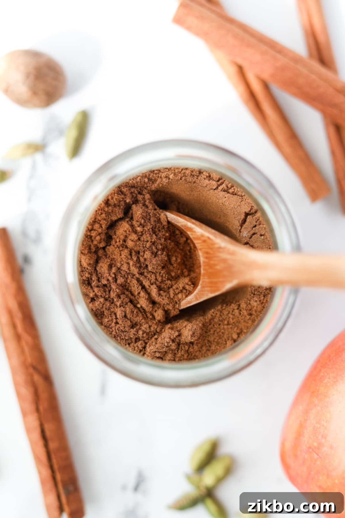 A small jar of apple pie spice with a small wooden spoon inside, evoking warmth and comfort.