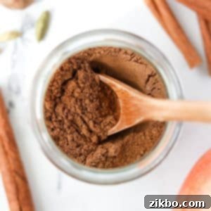 A small jar with a homemade spice blend and a wooden spoon inside, illustrating the finished apple pie spice.