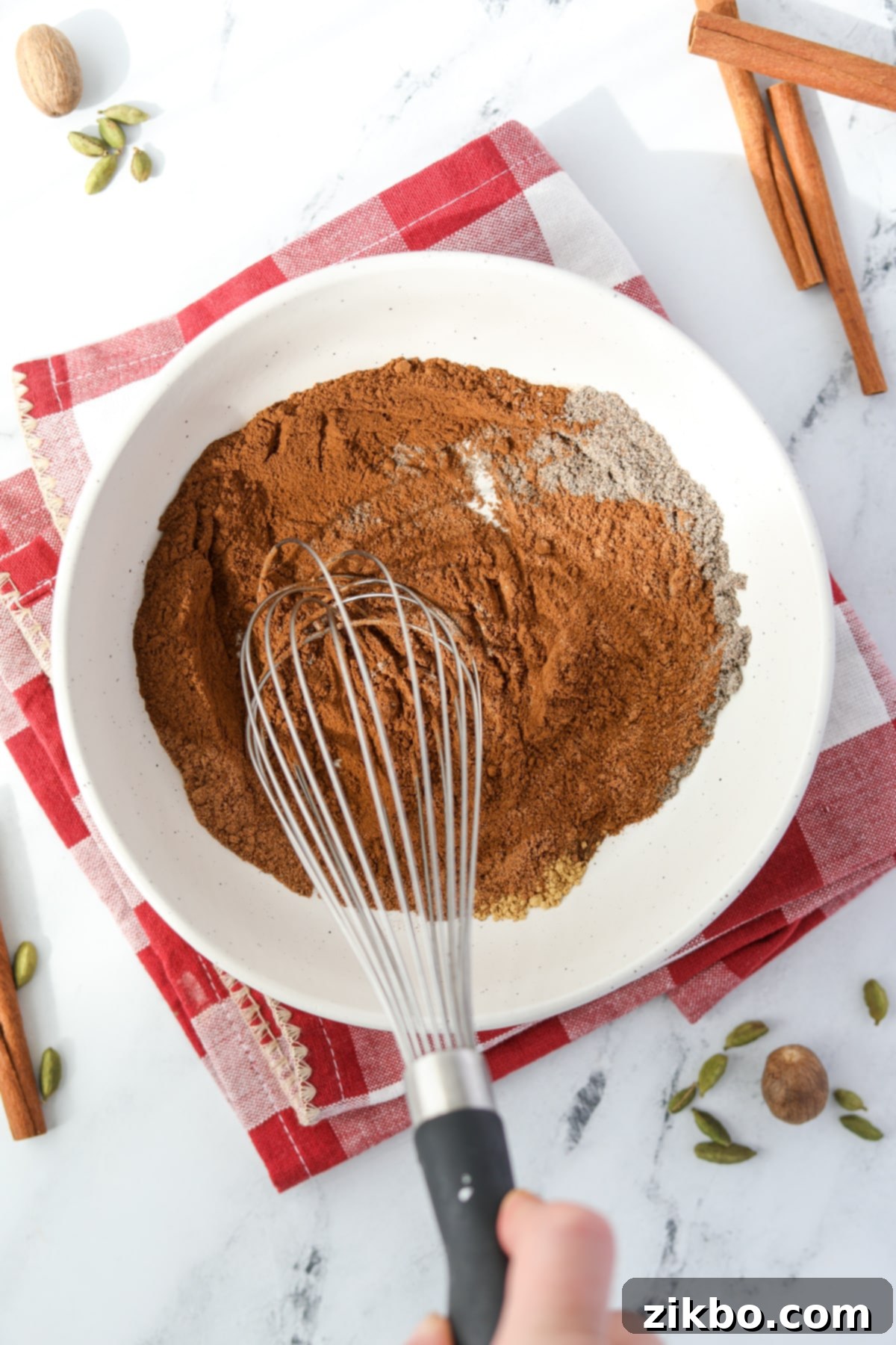 Whisking together various spices in a bowl to combine into a smooth, aromatic blend.