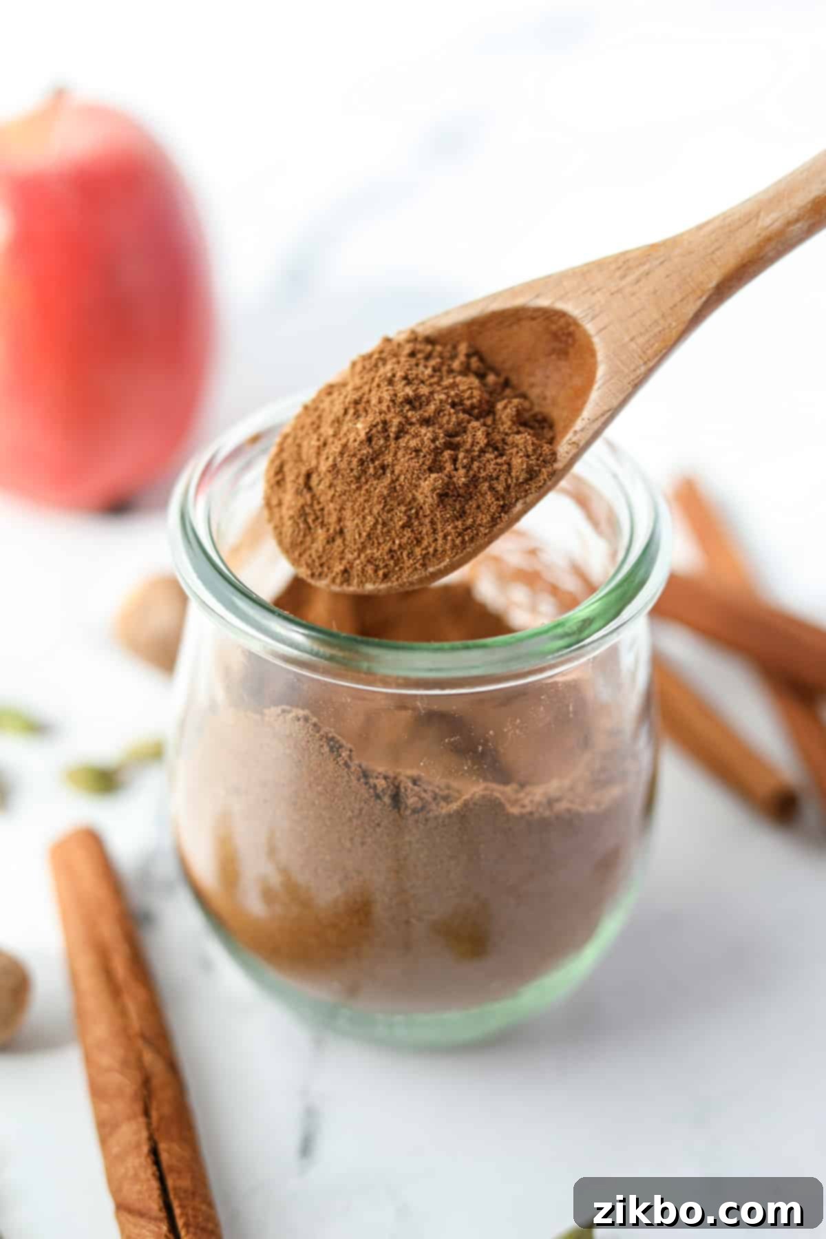 Using a spoon to take apple pie spice from a jar, highlighting its readiness for use.