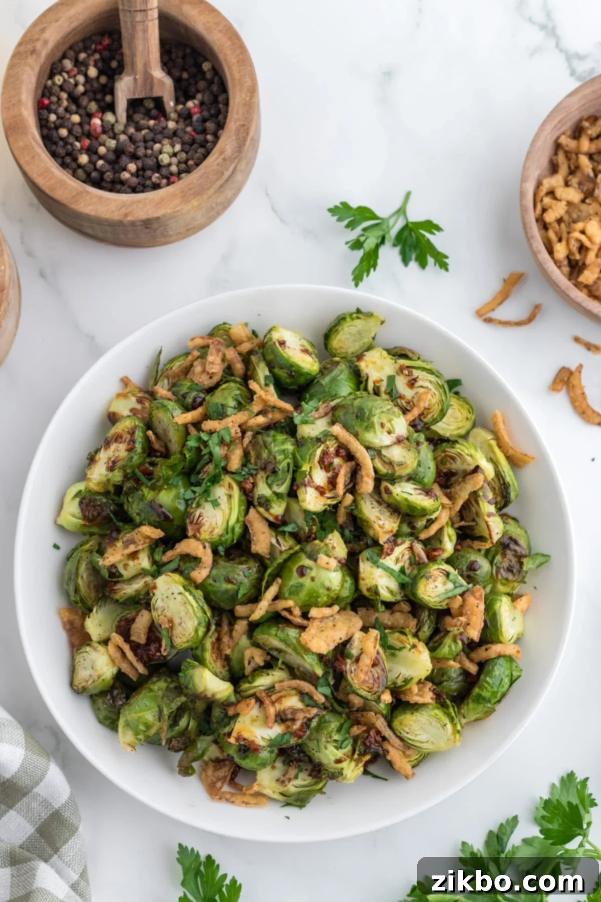 An overhead view of a serving bowl of cooked brussels sprouts with crispy onions and a glaze.