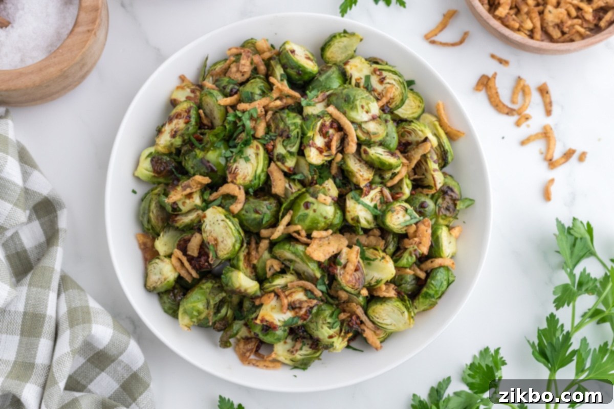 An overhead view of a serving bowl with roasted brussels sprouts, drizzled with glaze and topped with fried onions.
