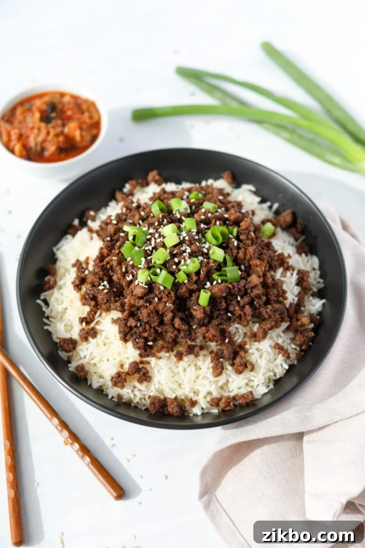 A vibrant bowl of white rice topped with seasoned Korean ground beef, garnished with fresh green onions and toasted sesame seeds.