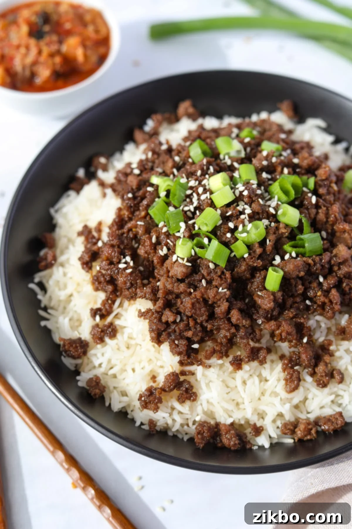 A visually appealing bowl of rice topped with Korean ground beef, garnished with fresh green onions and sesame seeds, ready to be enjoyed.