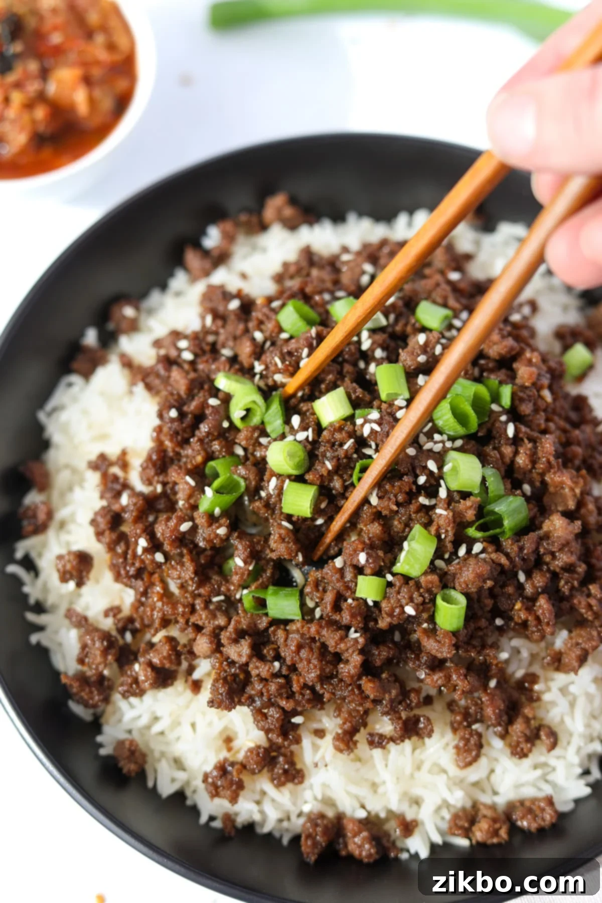 Chopsticks picking up a generous portion of Korean ground beef and rice from a bowl, highlighting the texture and appeal of the dish.