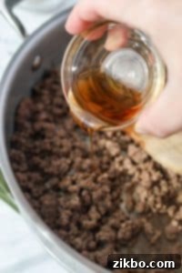 Sesame oil being drizzled into a skillet with cooked ground beef.