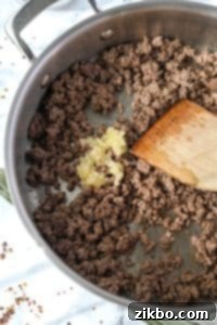 Minced garlic being added to a skillet with ground beef.