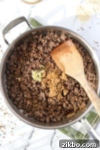 Ginger, soy sauce, and brown sugar being stirred into a skillet of ground beef.