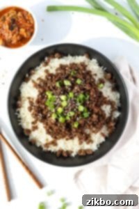 A bowl filled with rice and topped with seasoned ground beef, green onions, and sesame seeds.