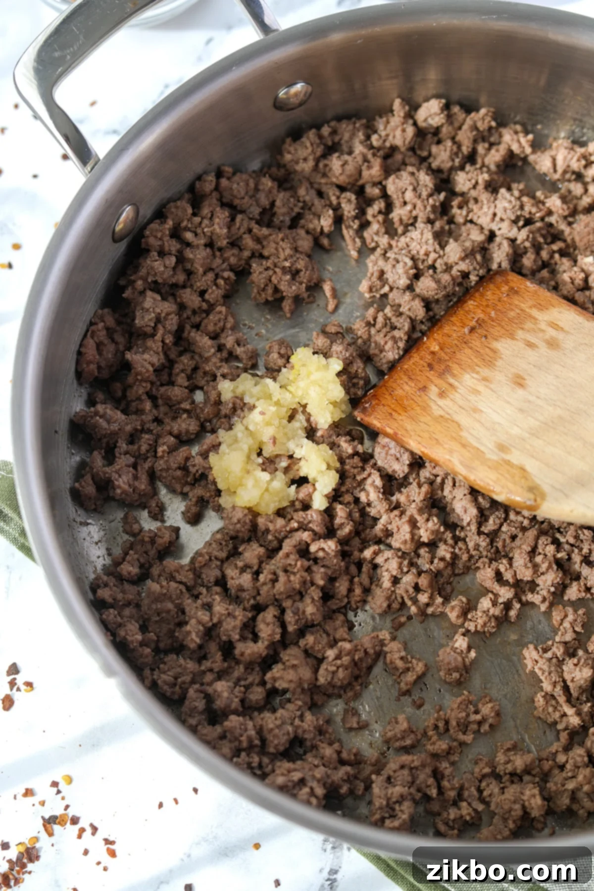 Minced garlic being added to browned ground beef in a skillet.