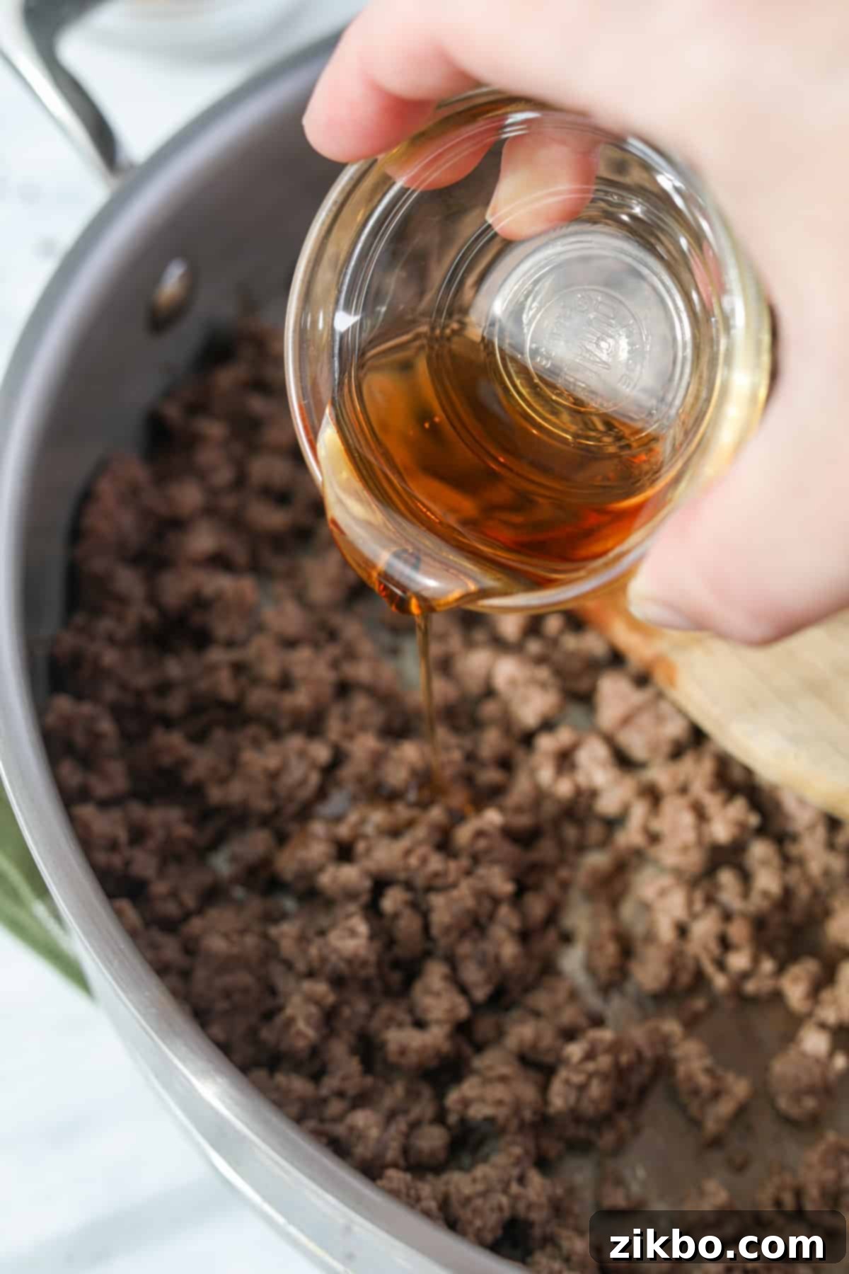 Sesame oil being drizzled into a skillet with cooked ground beef.