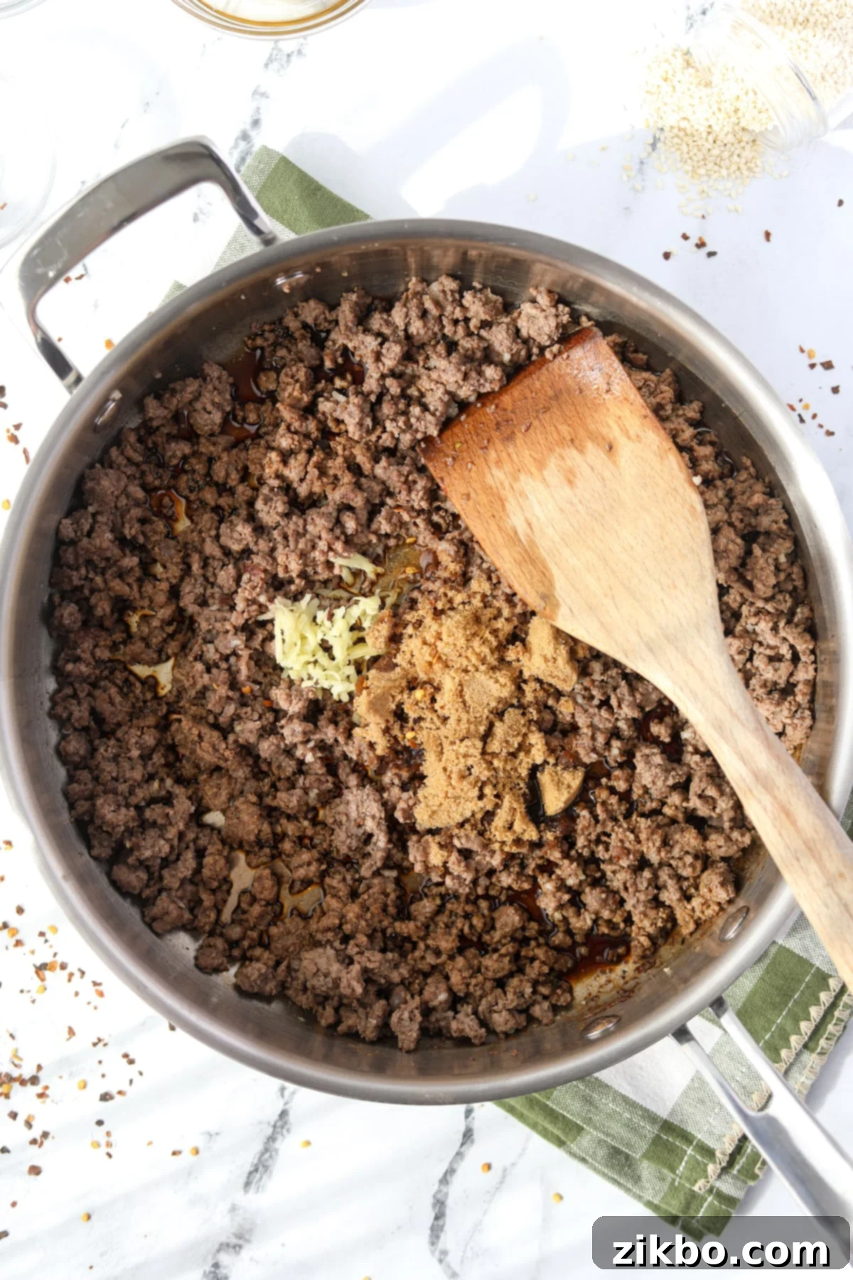 A mixture of ginger, soy sauce, and brown sugar being stirred into a skillet of ground beef.