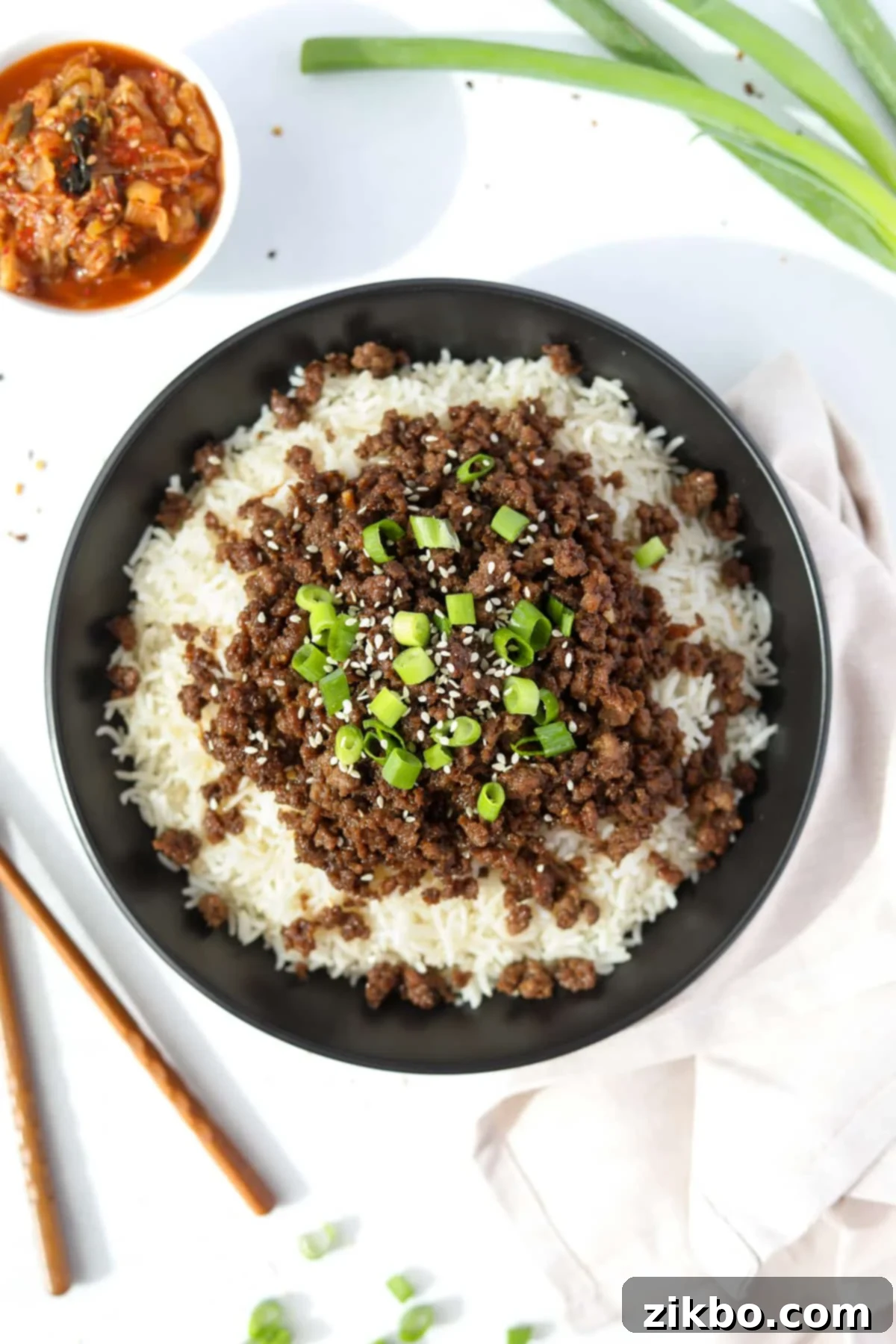 A beautifully arranged bowl filled with white rice, topped with savory Korean ground beef, garnished generously with vibrant green onions and sesame seeds.