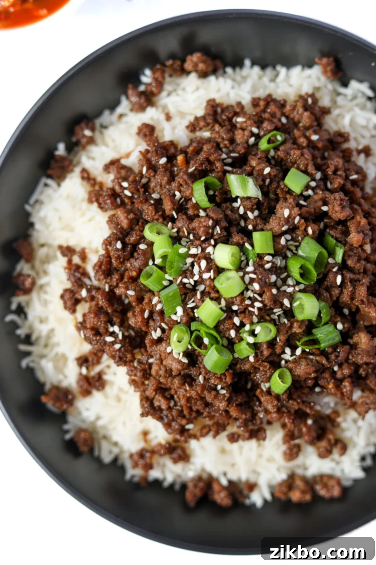 A close-up view of a bowl of white rice generously topped with homemade Korean ground beef, garnished with vibrant green onions and toasted sesame seeds.