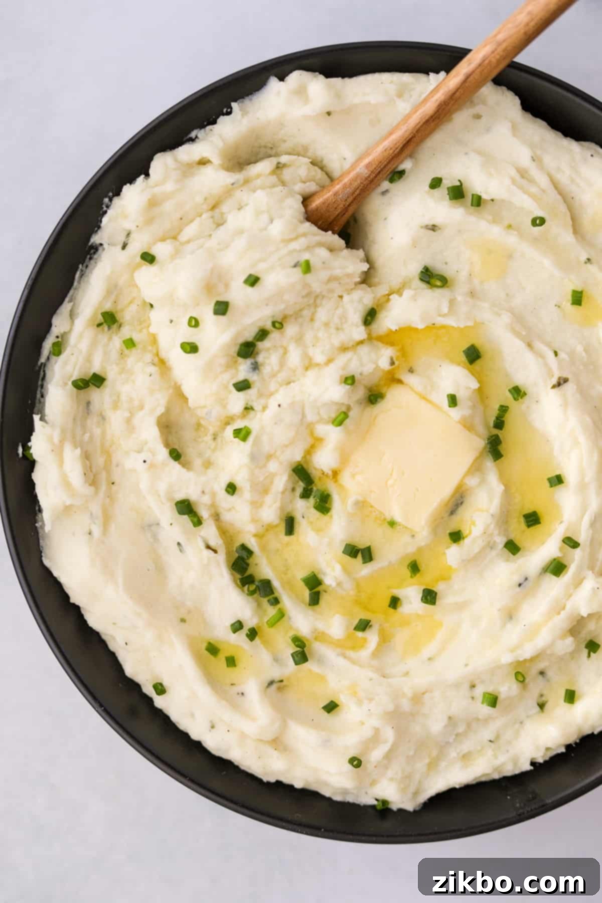 A black bowl filled with creamy Boursin mashed potatoes, topped with melted butter and fresh chives for garnish.
