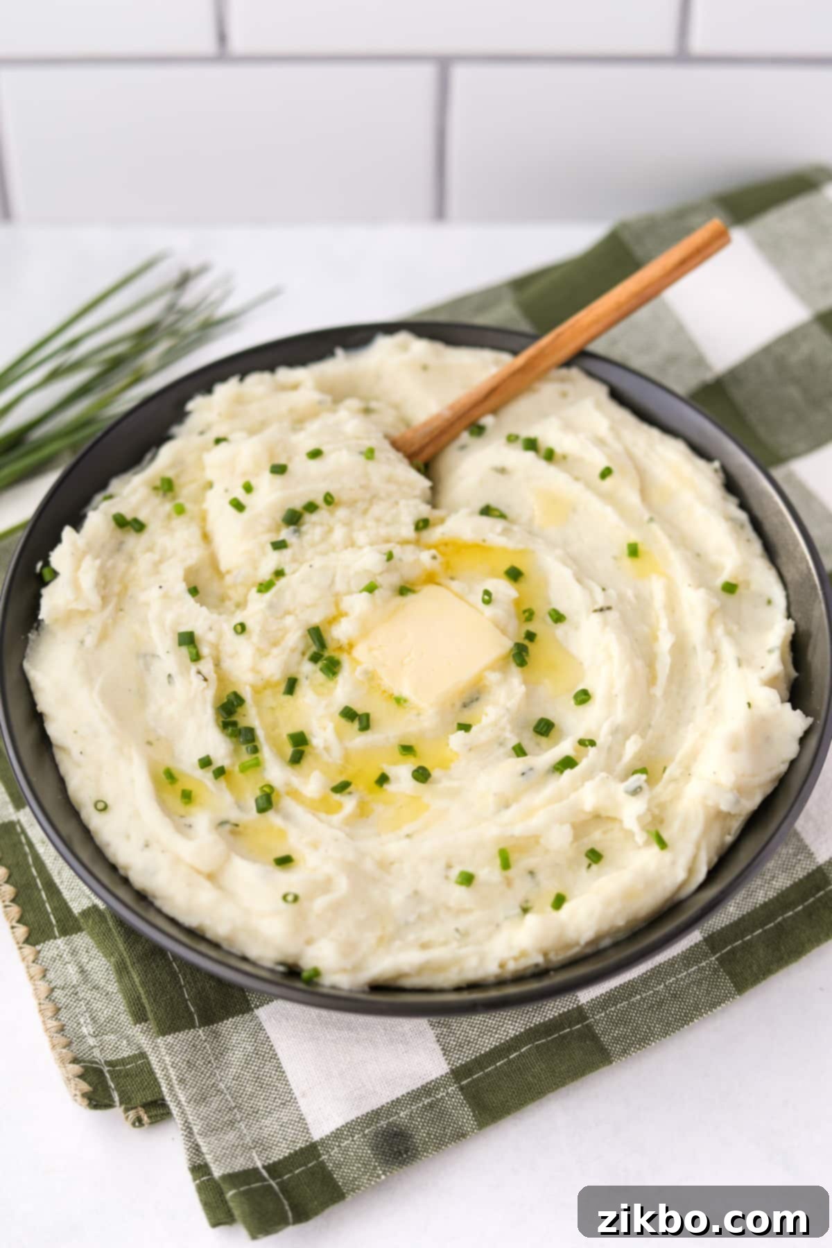 A large, rustic black bowl filled with creamy Boursin mashed potatoes, garnished with a single pat of butter and a generous sprinkle of fresh chopped chives.