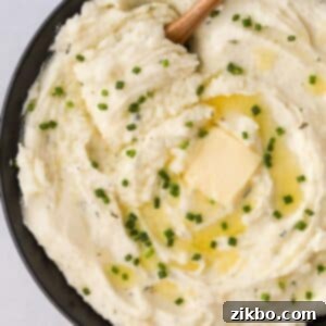 A close-up of a serving of Boursin mashed potatoes in a small black bowl, topped with melted butter and fresh chives.