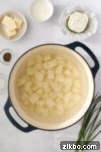 A dutch oven filled with uniformly cubed raw potatoes, ready to be boiled.