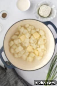 Cooked cubed potatoes returned to a large pot, with butter added and melting.